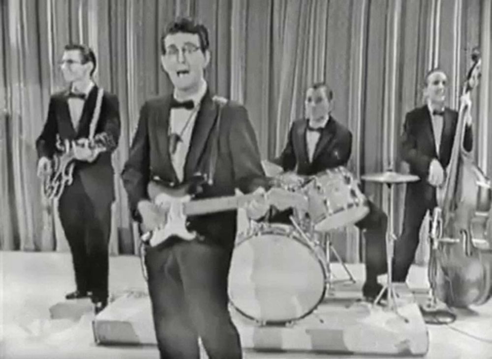 a black and white photo of a man playing a guitar in a band on a stage .