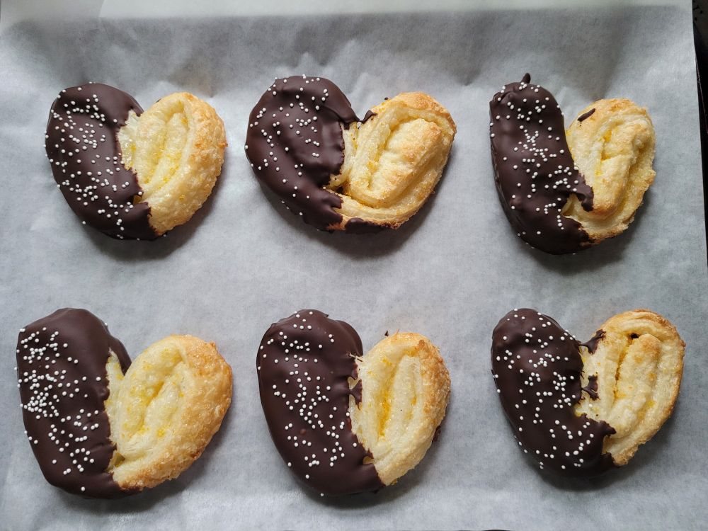 A tray of cookies, specifically palmiers with orange zest, dipped in chocolate with sprinkles. There are six on a tray.