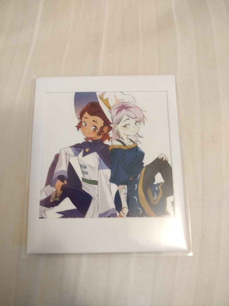 A card featuring Luz and Amity in their Halloween costumes patterned after Azura and Hecate, sitting back to back.