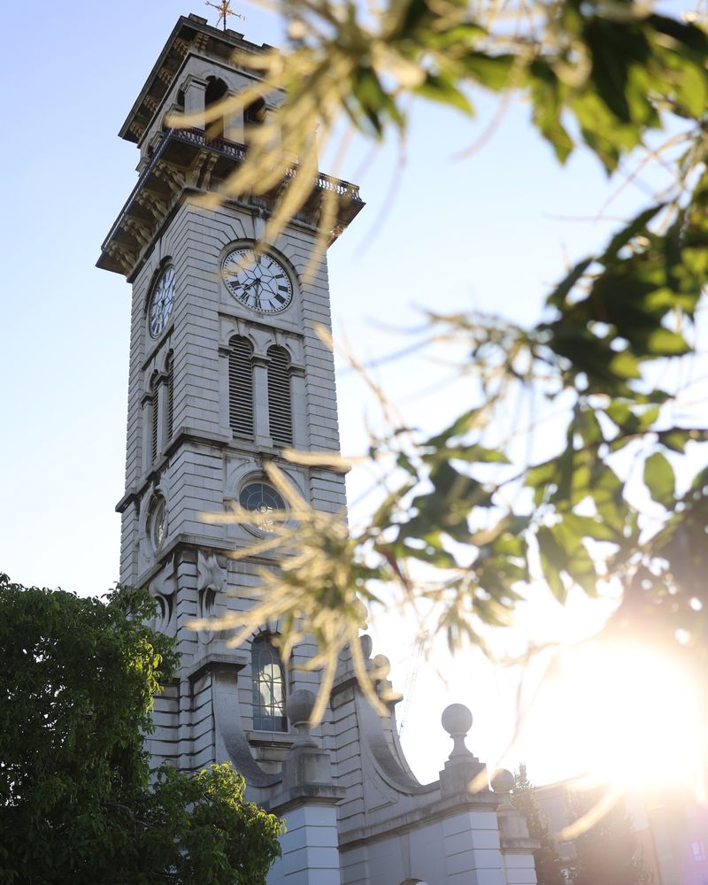 A picture of the Caledonian Clock Tower in Islington. The sun is going down and there are leaves from a tree reaching across the clock tower. 