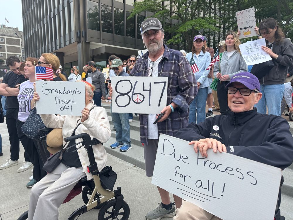 A man in a flannel shirt holds a sign with “8647” between his parents who are sitting in mobility aids. Their signs read “GRANDMA’S PISSED OFF!” and “DUE PROCESS FOR ALL!”
