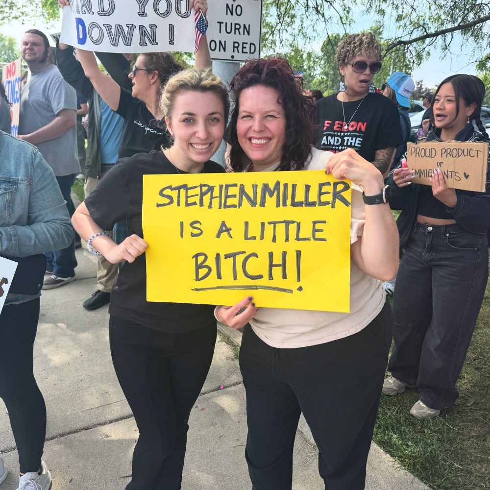 I’m standing next to a woman and we’re holding her sign together: “STEPHEN MILLER IS A LITTLE BITCH!”