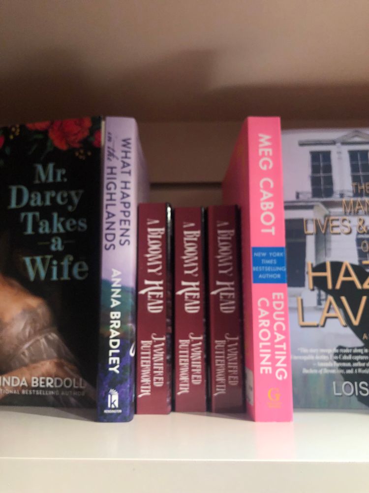 three maroon-spined copies of A Bloomy Head between What Happens in the Highlands by Anna Bradley and Educating Caroline by Meg Cabot