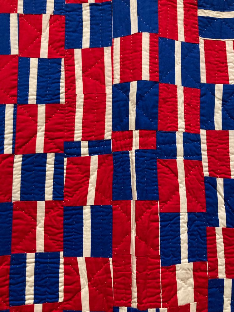 Close up of quilted square pieces sewn on diagonal lines adding yet another linear dimension to the rectilinear color patch composition 
