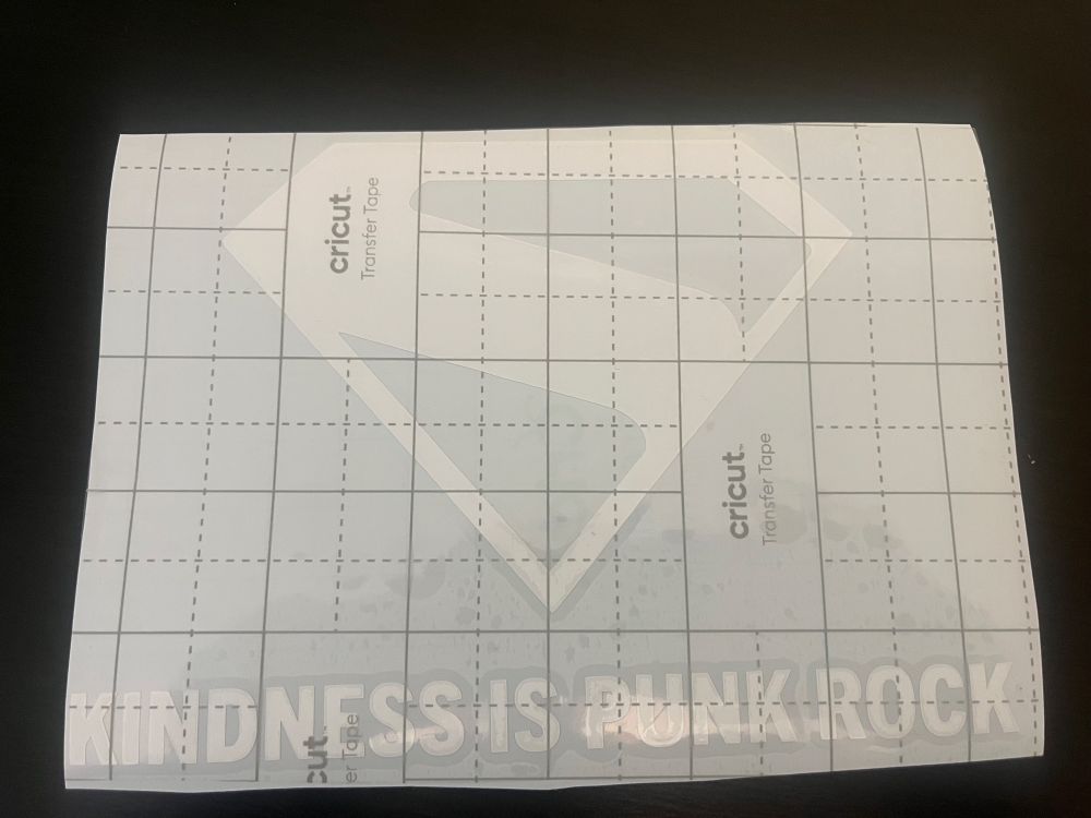 A vinyl white sticker with the 2025 S Superman logo with the subtext “kindness is punk rock”