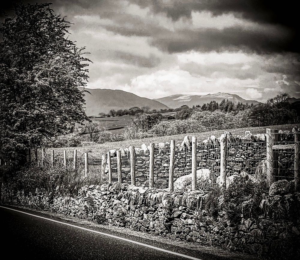 Rock wall behind a fence along a road with mountains in the distance 
