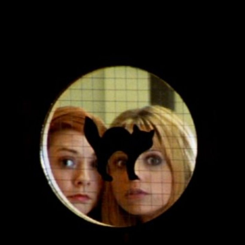 Buffy and Willow peering through a window with a cat sticker on it