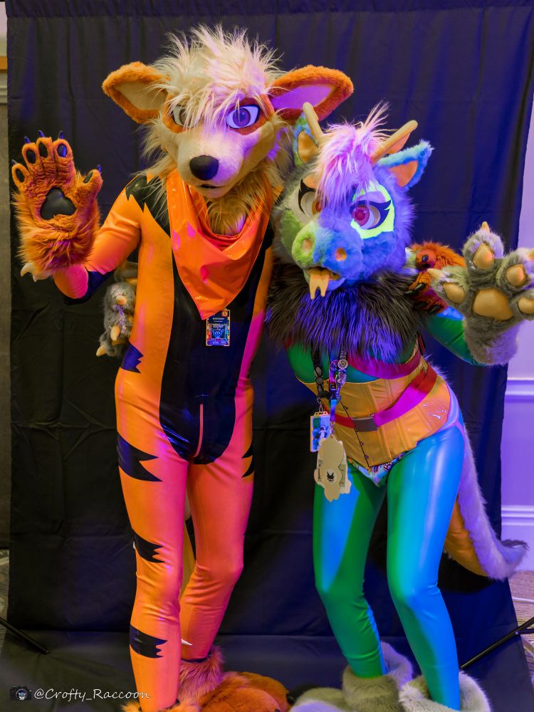 Two fursuiters pose for the camera. Orange Arcanine on the left and teal dragon on the right.

The Arcanine is wearing an Arcanine-patterned latex bodysuit and the dragon a teal latex bodysuit, both with fluffy paws and heads, the dragon is wearing a pink harness and yellow corset.