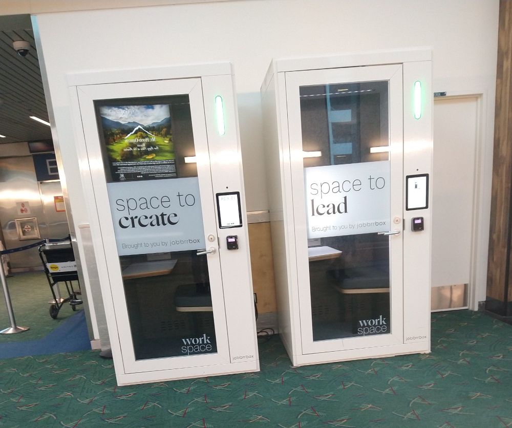Two phonebooth sized boxes labeled "work space" "space to create" "space to lead" in an airport hallway