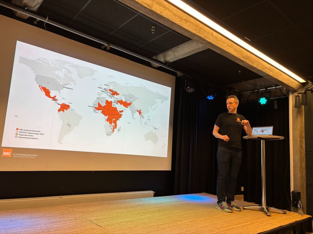 Man standing on stage behind podium with presentation in the background with maps