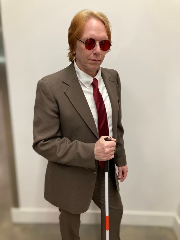 A middle-aged cosplayer, red headed, dressed up as comic accurate Matt Murdock.