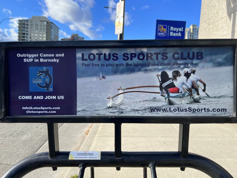 An ad attached to a bicycle rack, with a picture of people rowing an outrigger canoe. The copy reads "LOTUS SPORTS CLUB" and, as if a subtitle or slogan, "Feel free to play with the layout if you think it needs it"