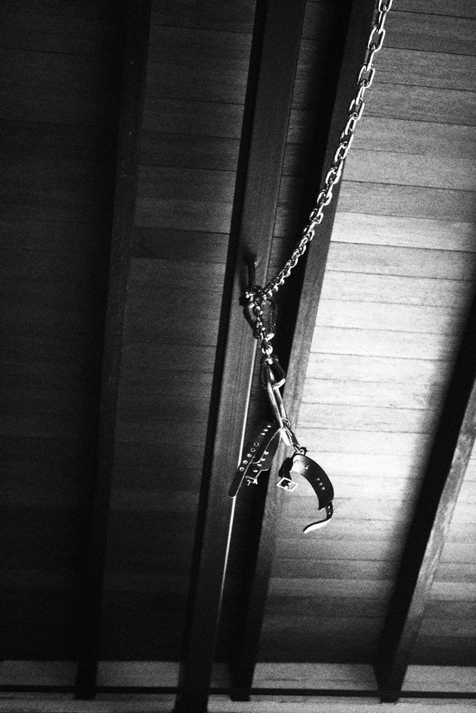 Chains, clips and leather cuffs hang from a hard point on the wooden ceiling, suggestively.