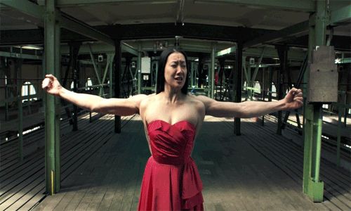 An animated GIF from the movie Pina, showing a woman in a red dress apparently flexing her arms; upon inspection we see that there's another person behind her who is in fact doing the arm thing.
