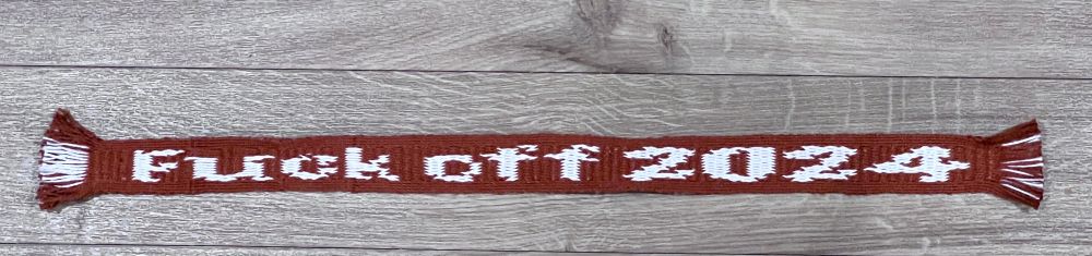 photograph, tablet woven band with text “Fuck off 2024” in white on a brown ground.