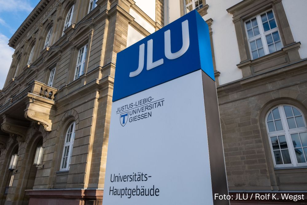 Stele mit der Aufschrift JLU und Hauptgebäude vor dem Hauptgebäude der Justus-Liebig-Universität Gießen.