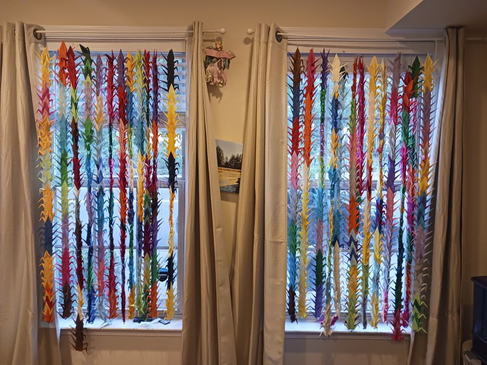 1000 multicolored origami cranes hanging in a pair of windows.