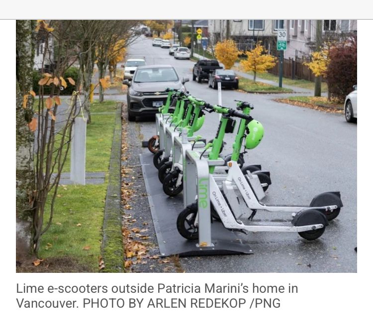 A row of scooters in docks on a street lined with parked cars on both sides 