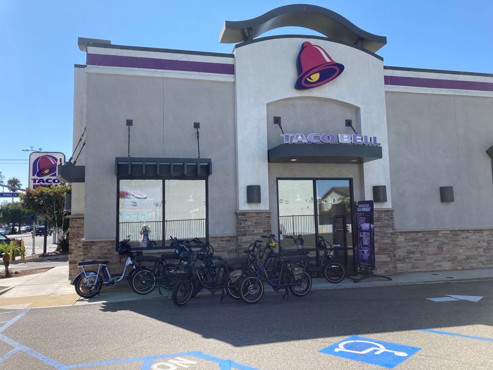 Taco Bell with 8 ebikes outside the door, on the shady side of the building 