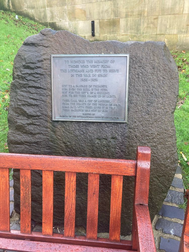 Large rock with memorial plaque behind a park bench 
