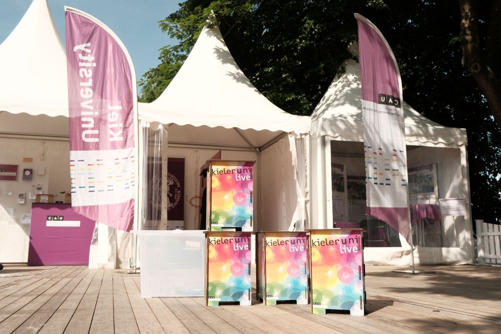 Eventzelte, Beachflags und bunte Hocker mit der Aufschrift Kieler uni live