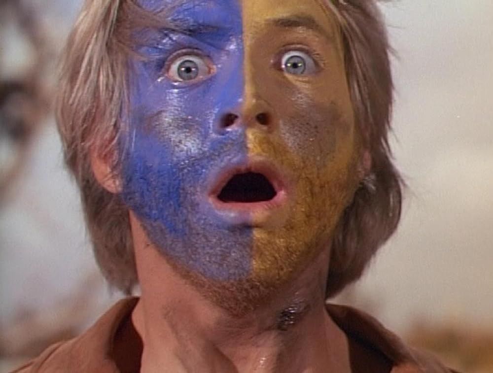 A stunned looking young man whose face is painted blue and yellow.