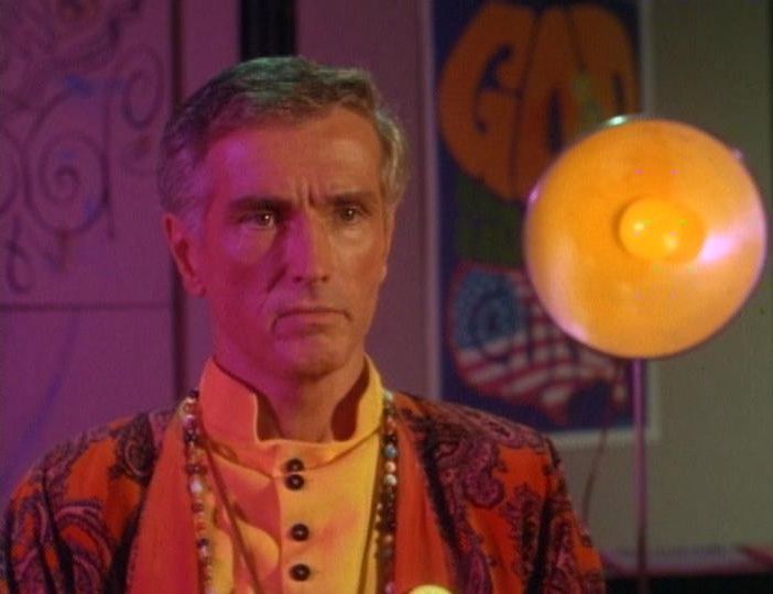 A guru wearing paisley 1960s clothes and beads, surrounded by psychedelic decor.