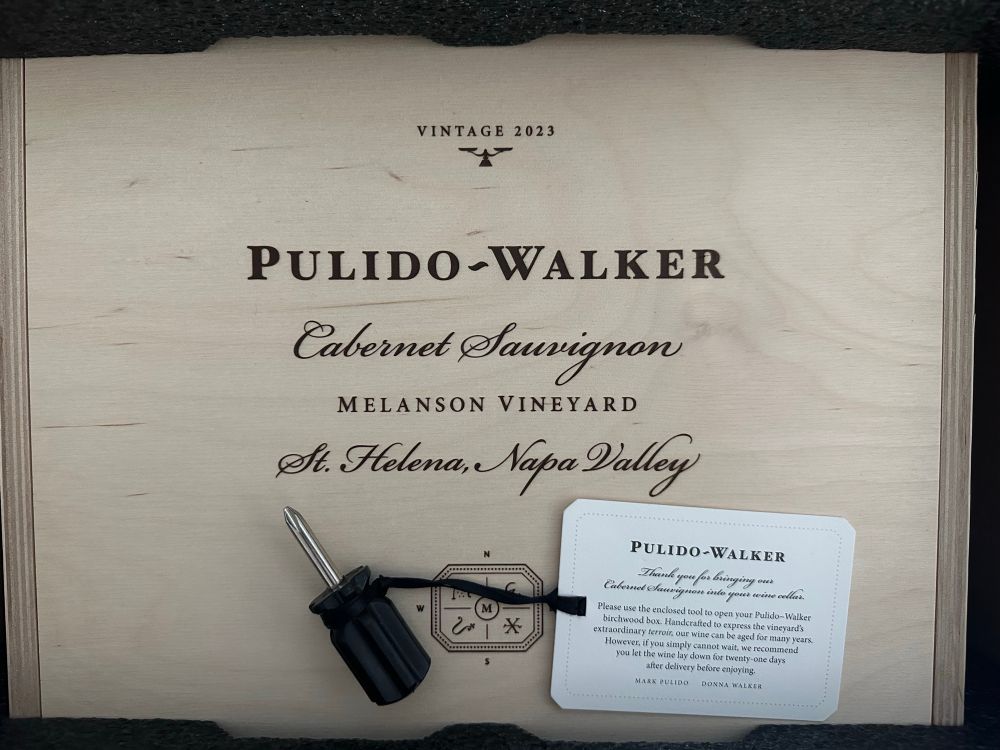 Photo of the top of a birchwood wine box of 2023 Pulido-Walker Melanson Vineyard cabernet sauvignon wine. A small Phillips-head screwdriver rests on top of it with a tag attached to it via a ribbon, saying:

Please use the enclosed tool to open your Pulido~Walker birchwood box. Handcrafted to express the vineyard's extraordinary terroir, our wine can be aged for many years.
However, if you simply cannot wait, we recommend you let the wine lay down for twenty-one days after delivery before enjoying.