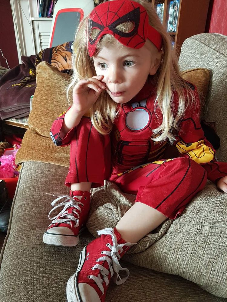 Young girl wearing an iron man costume and a Spiderman mask, with red converse and an intense expression.