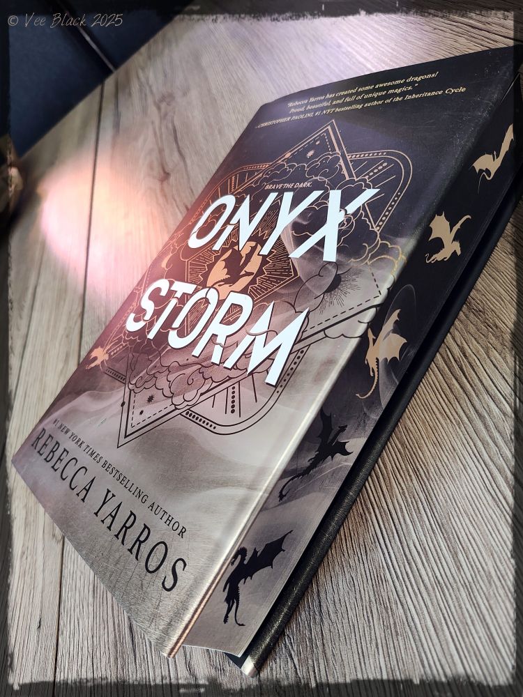 Book on a table. Picture in an angle so you can see the title and the sprayed edges with dragons in gold and black:
Onyx Storm Special Edition by Rebecca Yarros 
