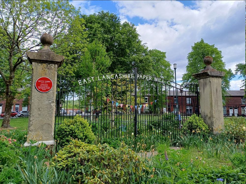 A picture of the old front gates of the East Lancashire Paper Mill Company. On the left of the gate on a column is a red heritage plaque that says:
BETTY TEBBS
1918-2017
Lifelong Activist
Peace Campaigner
Radical Working Class Hero
THE TIME FOR ACTION IS NOW!