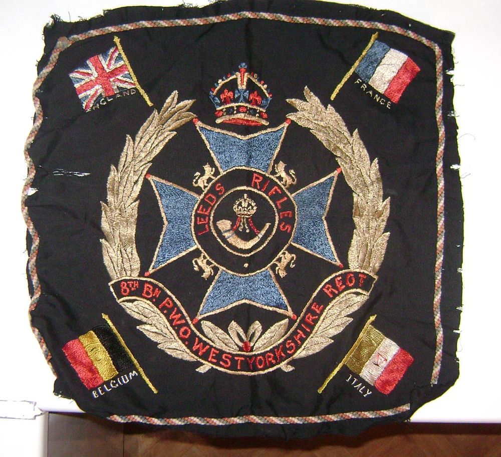 A photograph of a tapestry my grandfather made whilst convalescing after a shrapnel wound. It features insignia of the Leeds Rifles and the nations he fought beside - Belgium, France and Italy.