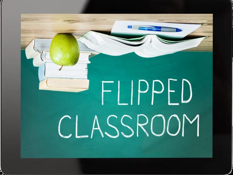An apple, pen, paper and books sitting on an upside down desk. Flipped Classroom written right side up on a chalkboard.