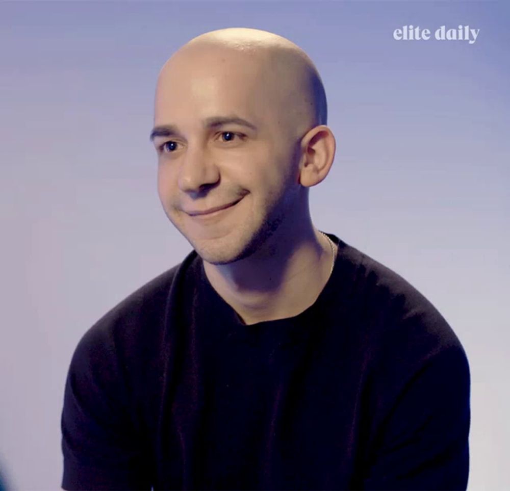 a bald man smiles in front of an elite daily logo