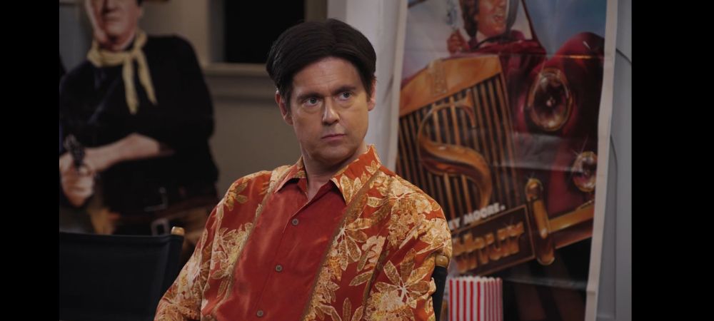 Newman wearing a red ornate button down shirt with a tasteful side parting of his sleek black hair