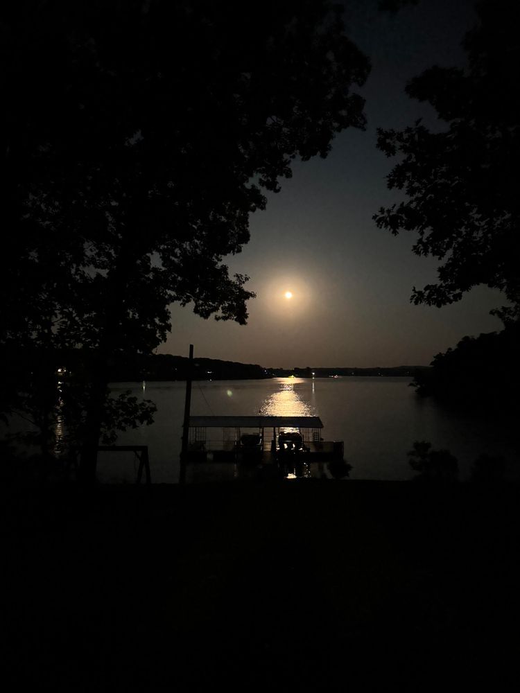 Photo of the full moon rising over Table Rock Lake with the shoreline and a dock in the foreground.