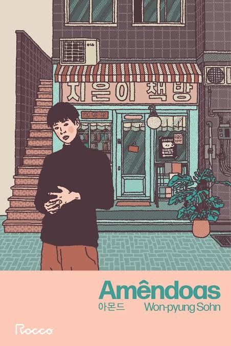 A capa ilustrada, com cores suaves e tons pastéis, mostra um jovem de blusa escura em primeiro plano, parado em frente a uma livraria ou café em estilo urbano (possivelmente coreano), com escadas externas à esquerda. O título "Amêndoas" e o nome do autor, "Won-pyung Sohn", aparecem em destaque na parte inferior, sobre um fundo rosa-salmão. A imagem tem uma atmosfera melancólica e introspectiva.