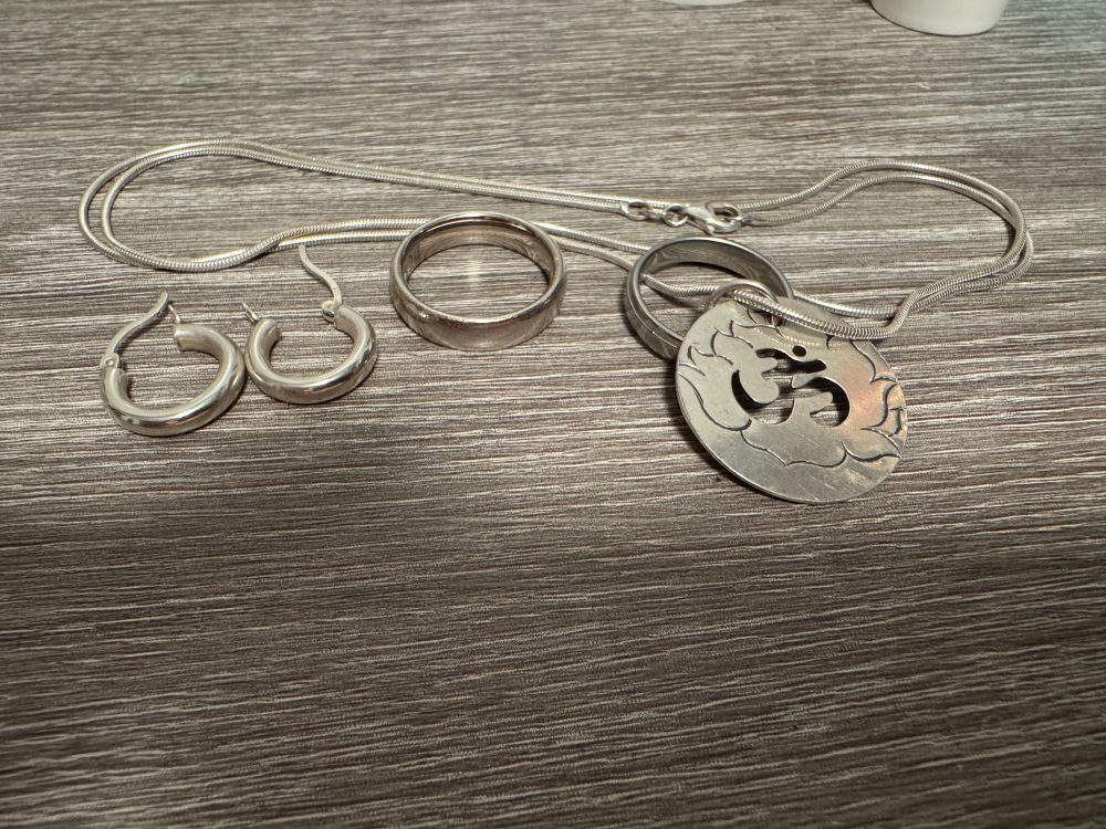 Die beschriebenen silbernen Schmuckstücke liegen auf einer grauen holzähnlichen Maserung. 
Die Ohrringe sind schlichte Kreolen und waren mal matt. 