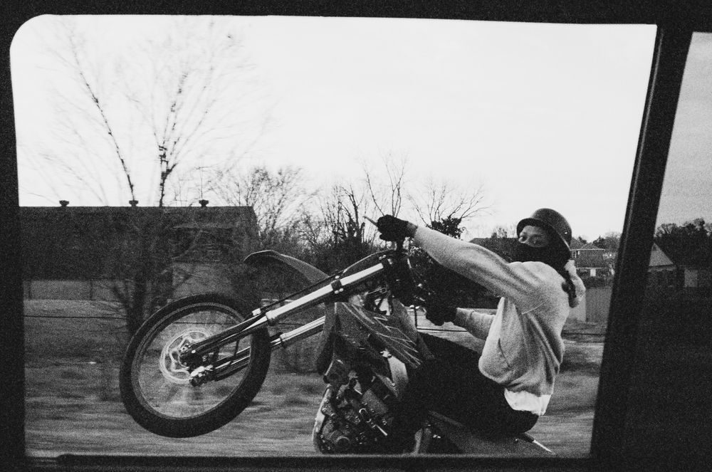 A black-and-white film photograph of a rider performing a wheelie on a motorcycle in an urban setting. The background features industrial buildings and parked buses, adding to the gritty, high-energy aesthetic. Captured on Kodak Tri-X, the motion blur emphasizes the dynamic and rebellious spirit of the scene.
Suggested Hashtags: #FilmPhotography #KodakTriX #MotorcycleLife #UrbanAesthetic #Wheelie #AnalogFilm #StreetPhotography
