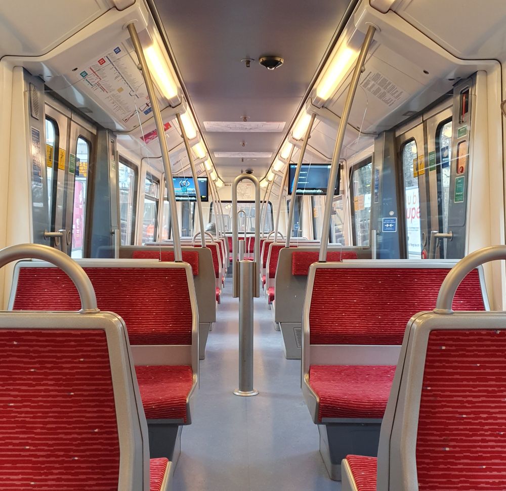 Blick in einen leeren U-Bahnwagen durch den mittleren Gang, rote Sitze, beige-graue Kunststoffverkleidungen.