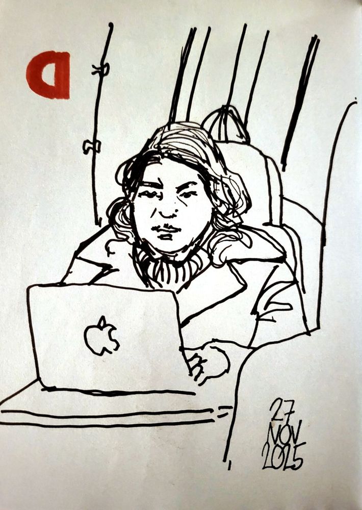 Kvinna i kappa på tåget. Sitter vid ett bord och skriver på sin laptop.