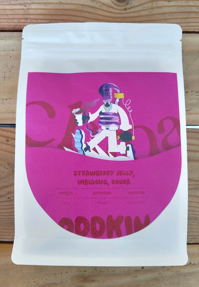 A white bag of coffee beans site on a pale wooden table. The bag has a large, luminous pink label with a. Illustration of a person walking with coffee. The person has a large pink snake swallowing their head.

The bag reads strawberry jelly, hibiscus, cocoa. Yunnan. Oddkin.