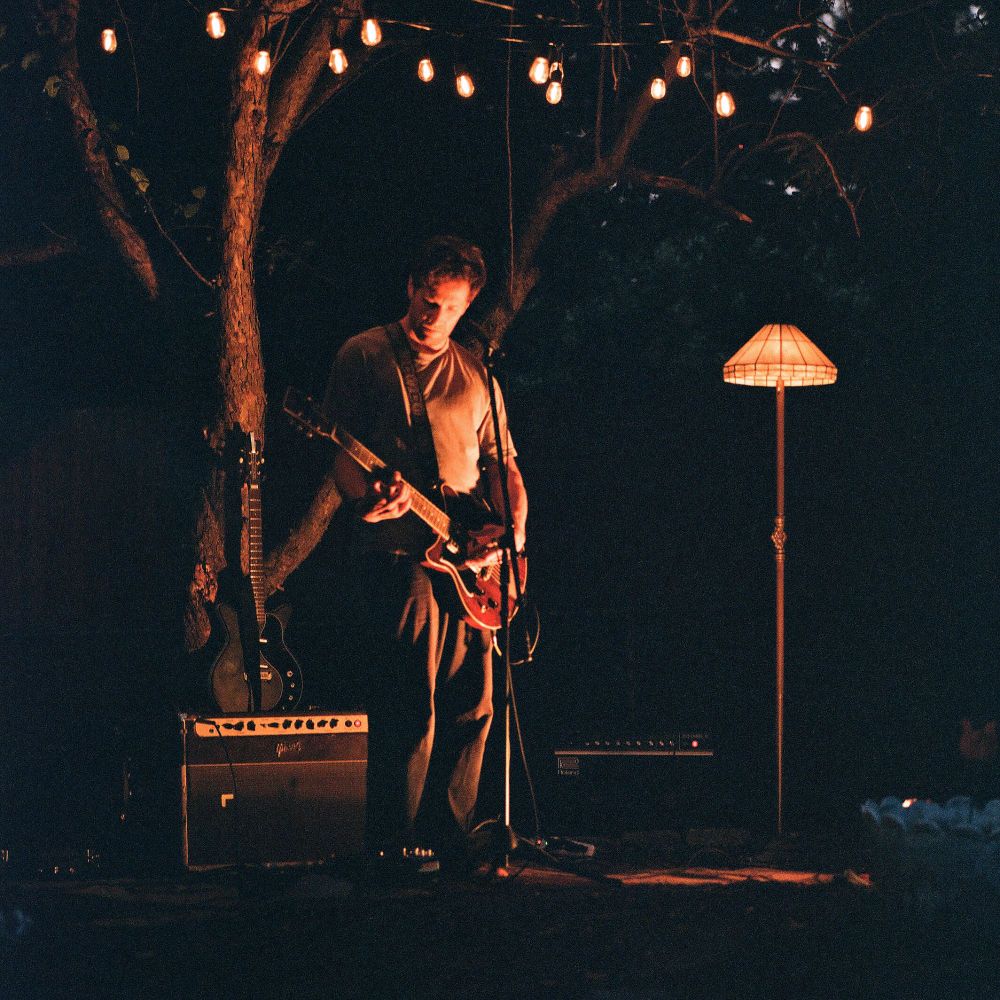 Rick Maguire from Pile playing guitar next to a lamp outside at dusk