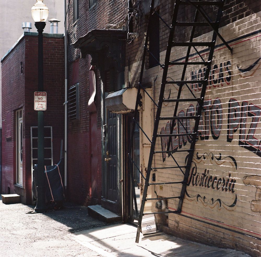 Photograph of an alleyway with a fire escape. The brick wall says Monica's Mercato Pizza
