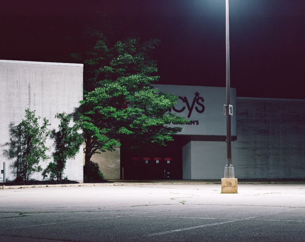 Night photograph of a lamp-lit mall façade with a tree partially blocking a Macy's sign