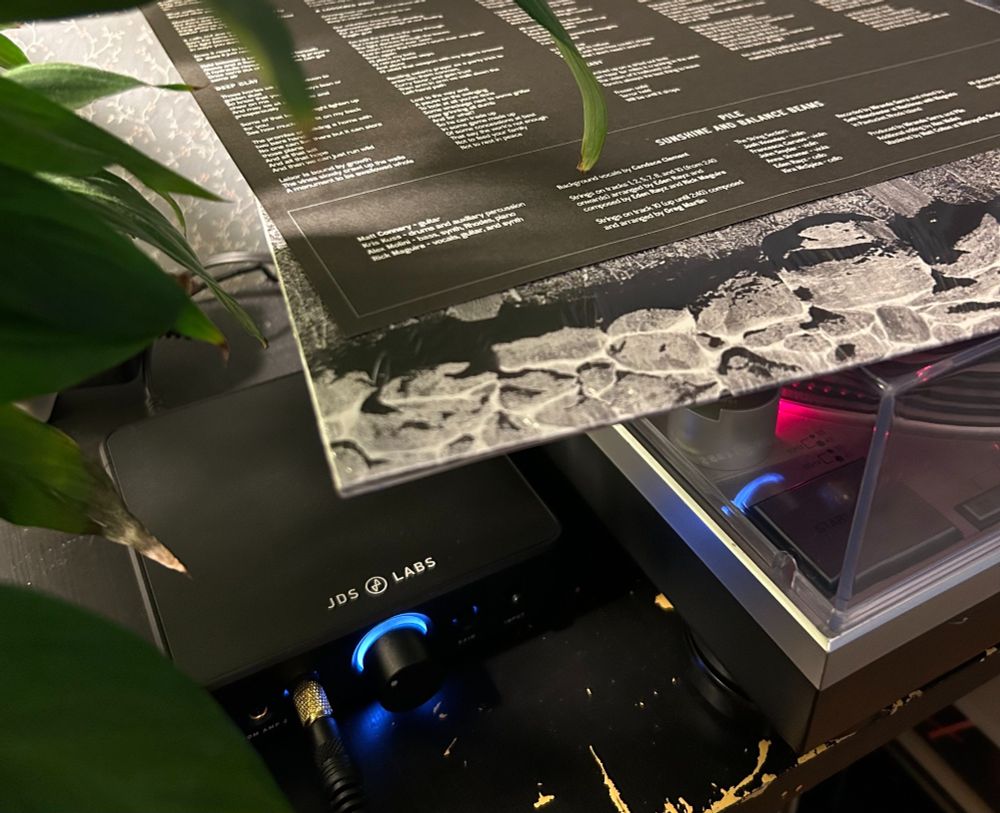 A record player spinning next to a headphone amp with the cover and liner notes of Pile's Sunshine and Balance Beams sitting on top