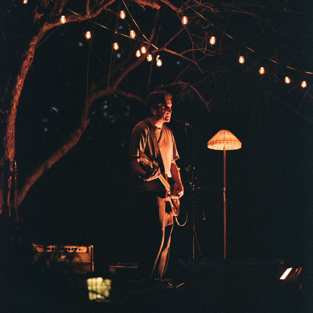 Rick Maguire from Pile playing guitar next to a lamp outside at dusk