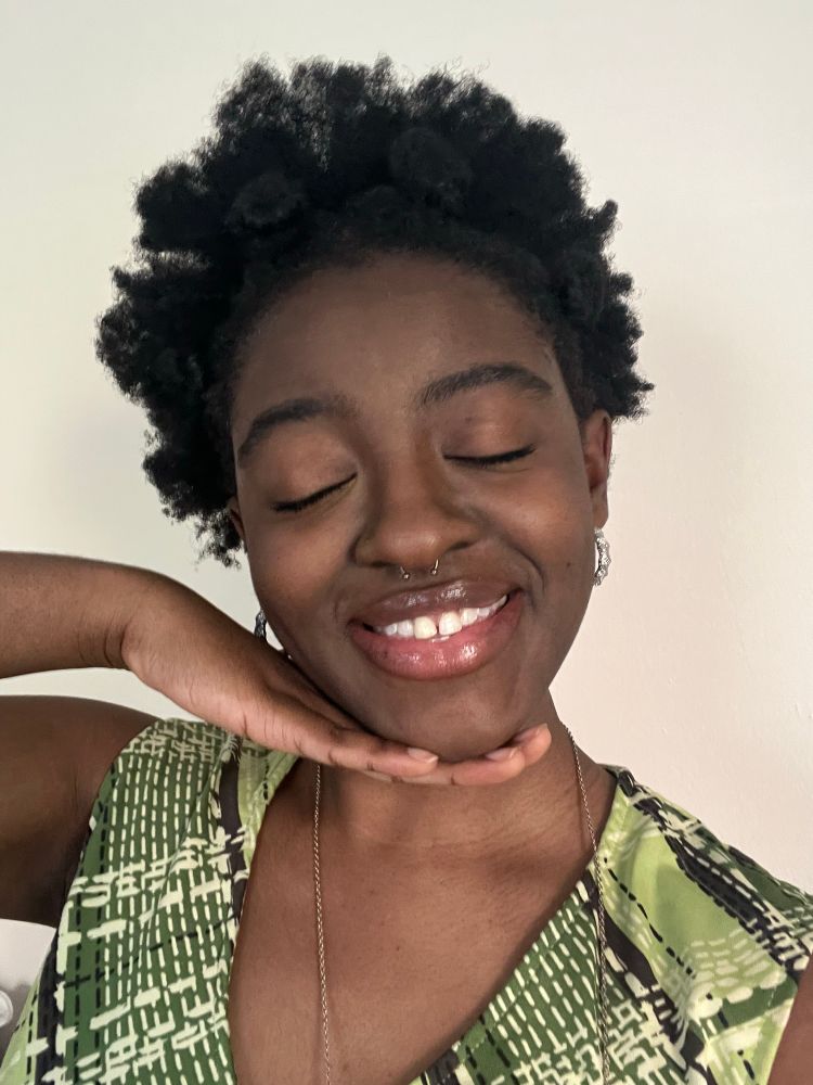 Astra smiling with hand underneath chin and eyes closed