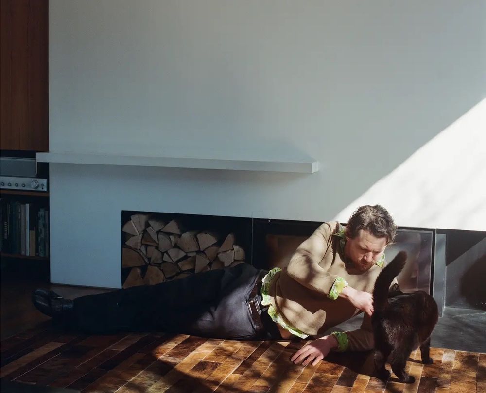 Jack O’Connell on the floor petting a black cat 