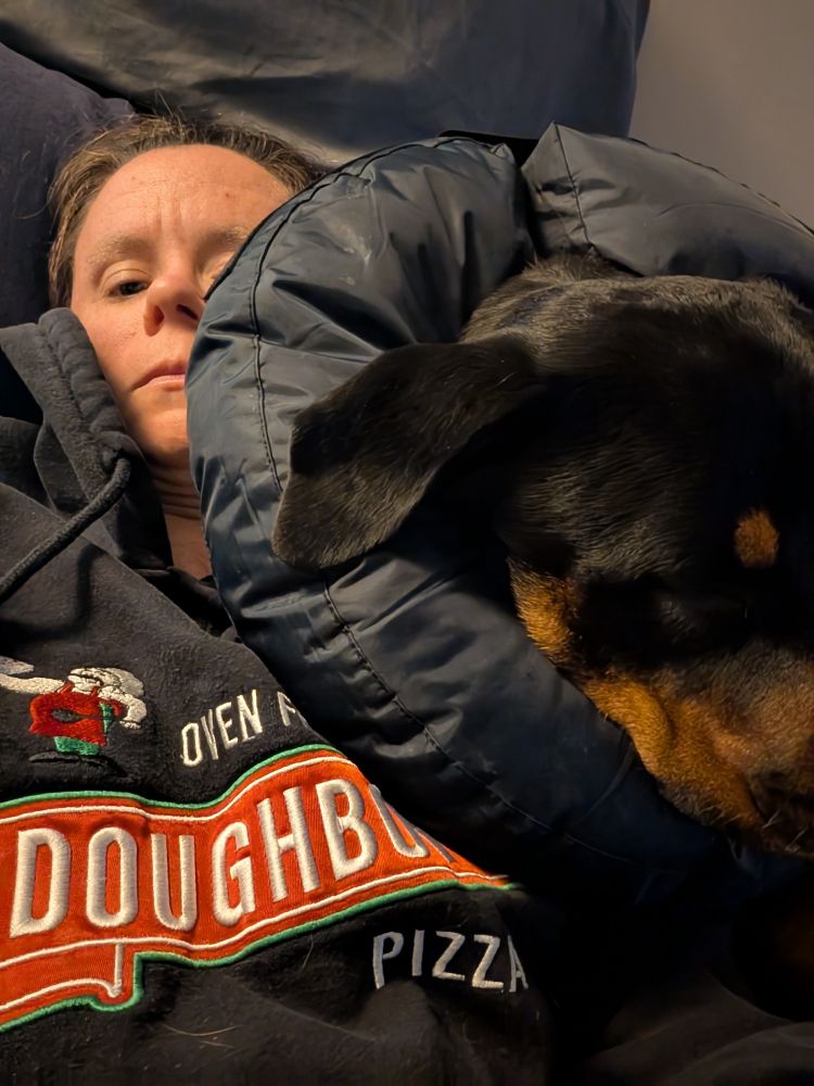 Rottweiler with a navy recovery donut around its neck that is covering half my face as we lay in bed.